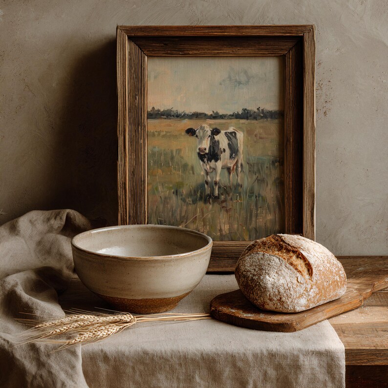 Cow print in wooden frame styled on rustic kitchen counter with bowl and artisan bread, warm farmhouse tones
