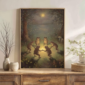 May include: A framed art print depicts six frogs dancing in a circle in a moonlit forest. The artwork features a warm color palette with a soft, dreamlike quality. The frogs are brown and tan, and the background includes trees, water, and glowing lights.