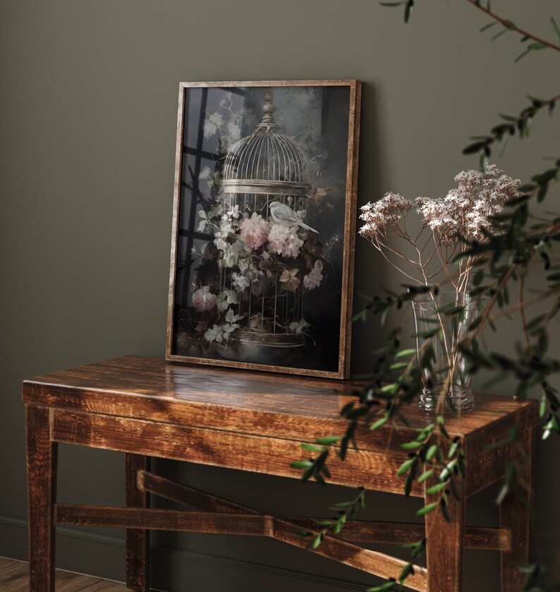 May include: A framed print of a bird in a cage surrounded by pink and white flowers. The cage is made of metal and has a delicate design. The background is a dark green color.