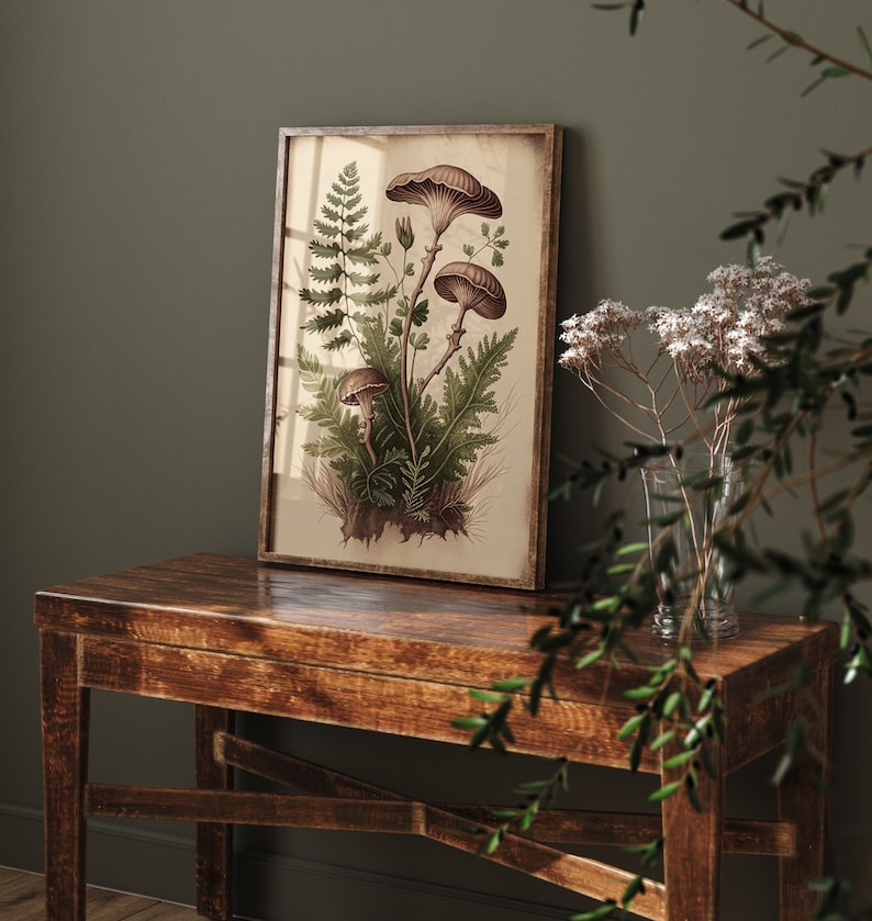 May include: A framed botanical print featuring a cluster of brown mushrooms and green ferns on a cream background. The print is displayed on a dark brown wooden table.