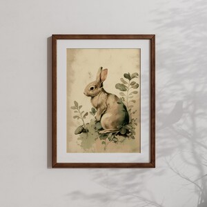 Pu&ograve; includere: Un'illustrazione vintage incorniciata di un coniglio marrone seduto in un ciuffo di foglie verdi. Lo sfondo &egrave; beige chiaro con un effetto acquerello.