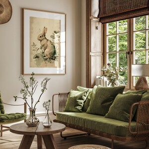 Pu&ograve; includere: Un divano in velluto verde con una struttura in rattan intrecciato si trova in un soggiorno con una stampa incorniciata di un coniglio, un tavolino da caff&egrave; in legno e uno sgabello intrecciato.