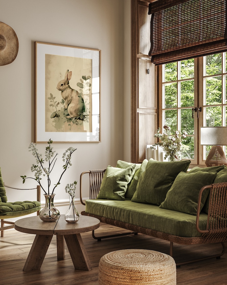 Pu&ograve; includere: Un divano in velluto verde con una struttura in rattan intrecciato si trova in un soggiorno con una stampa incorniciata di un coniglio, un tavolino da caff&egrave; in legno e uno sgabello intrecciato.