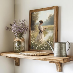 May include: A wooden shelf with a framed painting of a woman in a white dress standing in a field of flowers. A mason jar filled with purple flowers, a woven placemat, and a metal watering can are also on the shelf.