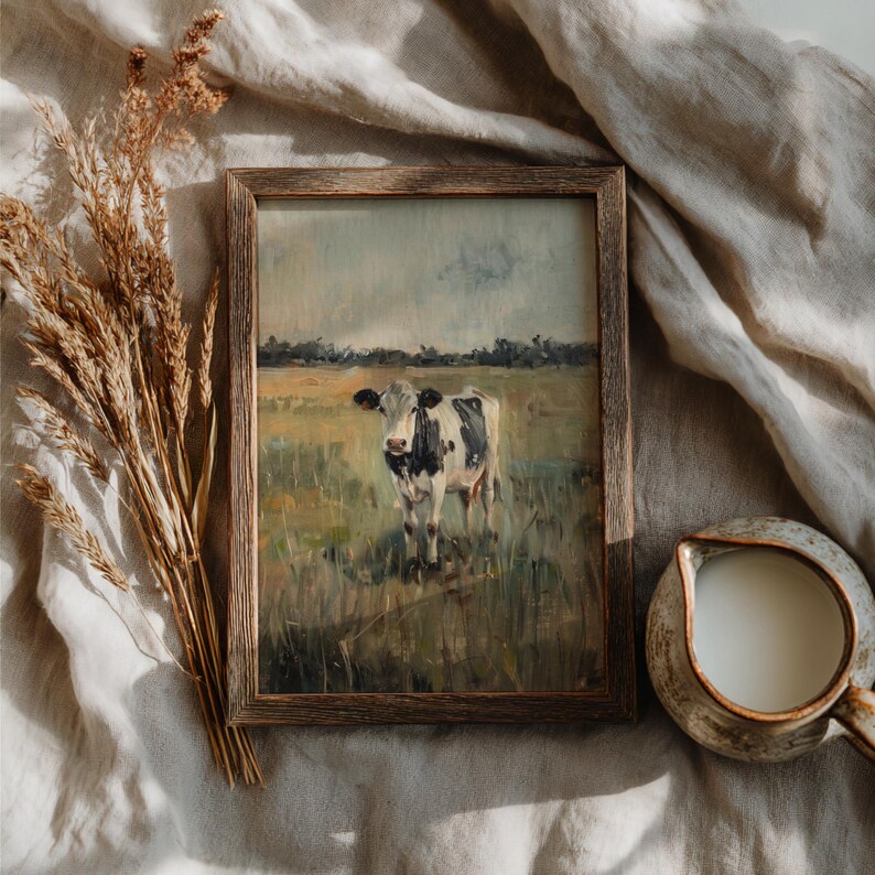Top view of vertical rustic frame with cow artwork on linen cloth, paired with dried florals and warm ceramic mug