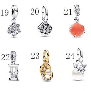 Puede incluir: Una colecci&oacute;n de abalorios plateados y dorados. Los abalorios incluyen una flor con piedras transparentes, una concha con piedras transparentes, un abalorio de color coral, un reloj de arena, un abalorio con una perla y piedras transparentes, y un abalorio con un &aacute;ngel y una perla.