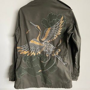 May include: A green military-style jacket with a gold and white embroidered crane design on the back.
