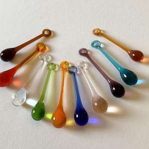 Peut inclure: Un ensemble de 12 ornements en verre en forme de goutte avec une boucle en haut. Les ornements sont de différentes couleurs, notamment transparent, orange, rouge, vert, bleu et violet.