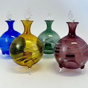 Op de afbeelding: Vier glazen flessen met decoratieve swirl-patronen en vlinderstoppen. De flessen zijn in blauw, geel, groen en paars.