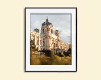 May include: A large, pale yellow building with a central dome and multiple towers. The building is surrounded by green trees and bushes. The building is lit by the warm glow of the setting sun.