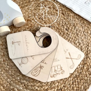 May include: Wooden baby milestone markers with golf-themed illustrations. Each marker is engraved with a different golf-related image and the words "newborn" and "months". The markers are arranged in a fan shape.