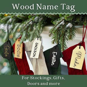 May include: Five wooden name tags with different names written on them, hanging from stockings. The names are Jackson, Bodie, Greta, Meda, and Easton. The text below the tags reads "For Stockings, Gifts, Doors and more".