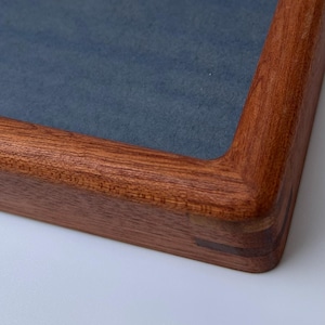 May include: Close-up of a wooden picture frame with a dark blue interior. The frame is made of reddish-brown wood with rounded corners and visible joinery. The frame is on a white surface.
