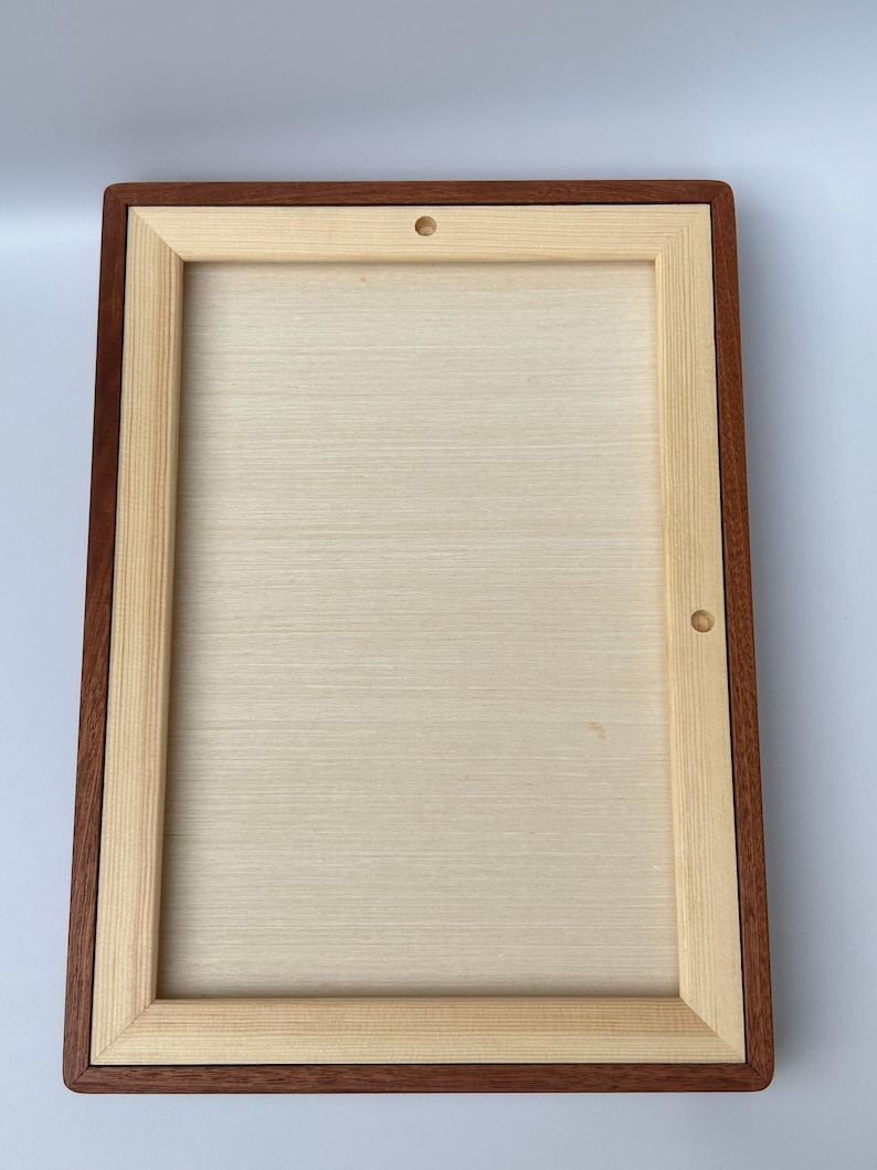 May include: A rectangular wooden frame with a light-colored interior and a dark brown border. The frame has a natural wood grain appearance and two small holes on the top and side.