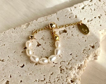 May include: A gold adjustable ring with a chain and a small oval tag that says "mila". The ring is adorned with a row of white pearls.