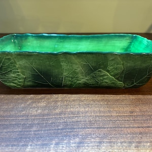 Op de afbeelding: Een groene keramische bakvorm met een bladontwerp. De vorm is rechthoekig en gemaakt van geglazuurd keramiek.