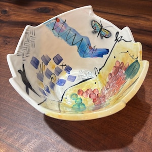 May include: A white ceramic bowl with a unique, abstract design. The bowl features a butterfly, a woven pattern, and colourful swirls and dots.