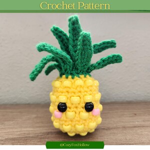 May include: A crocheted pineapple with a smiling face, featuring yellow body, green leaves, and black eyes. The text "Crochet Pattern" is at the top, and "@CozyFoxHollow" is at the bottom. The pineapple is a handmade craft.