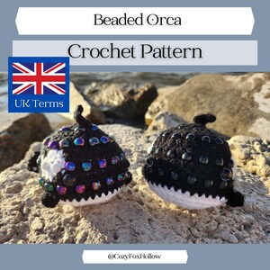 May include: Two crocheted orca whales with black bodies, white bellies, and iridescent beaded accents. The image includes text that reads "Beaded Orca Crochet Pattern" and the UK flag.