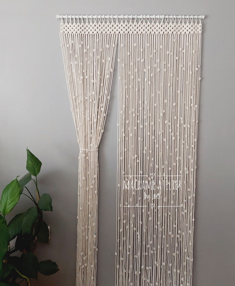 K&ouml;nnte beinhalten: Ein wei&szlig;er Makramee-Vorhang mit Perlenmuster h&auml;ngt an einer wei&szlig;en Stange. Der Vorhang ist aus Baumwollschnur gefertigt und hat einen schlichten, minimalistischen Stil. Der Text "MACRAME  ATELIER by LNES" ist in der unteren rechten Ecke des Bildes sichtbar.