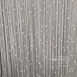 K&ouml;nnte beinhalten: Ein wei&szlig;er Makramee-Wandbehang mit einem sich wiederholenden Knotenmuster. Der Behang ist aus dickem Baumwollschnur gefertigt und hat eine subtile Textur. Der Text "MACRAME ATELIER" ist in der rechten unteren Ecke des Bildes sichtbar.