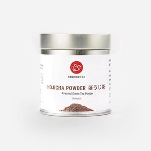 May include: A cylindrical metal container of Hojicha powder, a roasted green tea powder. The label features the text "SENBIRDTEA" and "HOJICHA POWDER" in English and Japanese. A red bird logo is also visible. The container is filled with brown tea powder.