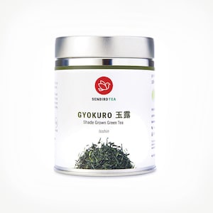 May include: A cylindrical metal container of Gyokuro shade-grown green tea. The label features the text "SENBIRD TEA" and "GYOKURO 玉露 Shade Grown Green Tea". A red logo of a bird is above the text. A pile of green tea leaves is visible at the bottom.