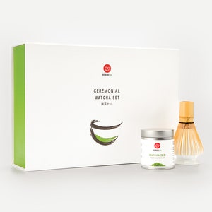 May include: A white box with green trim and the text "Ceremonial Matcha Set" on the front. The box contains a silver tin of matcha powder, a bamboo whisk, and a white ceramic bowl.