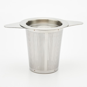 May include: A stainless steel tea infuser with a perforated cylindrical basket and two small handles. The infuser is designed to sit inside a mug or teapot for steeping loose leaf tea. The infuser is shown against a white background.