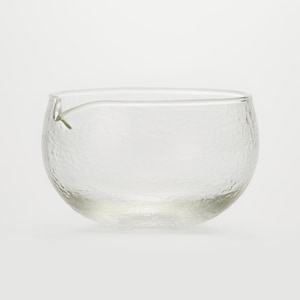 May include: A clear, textured glass bowl with a spout. The bowl has a rounded shape and a slightly rough surface. The spout is small and delicate, extending from the rim. The glass is transparent, allowing light to pass through.