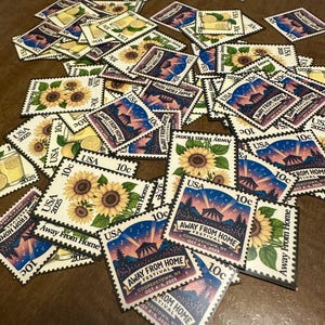 May include: A pile of USA postage stamps with floral and festival designs. The stamps display "10c" and "USA", with some advertising the "Away From Home Festival, Cooperstown, NY, Oct 4-5, 2025".