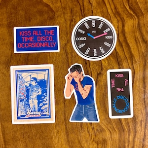 May include: A collection of stickers with various designs and text. One sticker reads "KISS ALL THE TIME. DISCO, OCCASIONALLY." Another features a clock with "KISS" around the edge. Other stickers include illustrations and text.