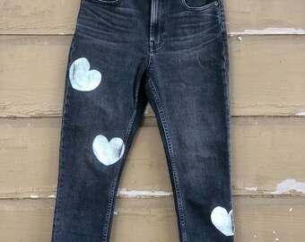 May include: Dark wash denim jeans with white heart-shaped designs on the legs.