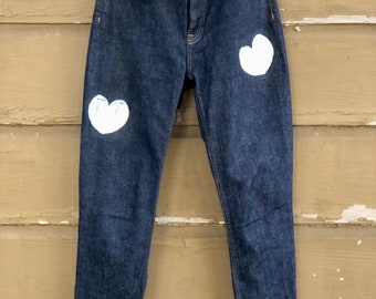 May include: Dark blue denim jeans with white painted hearts on the front of the legs.