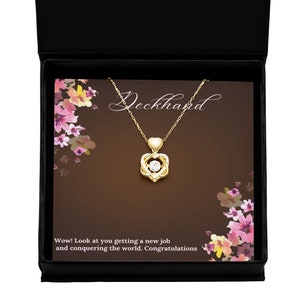 May include: A gold necklace with a spinning heart pendant featuring a clear crystal. The necklace comes in a black box with a card that reads "Deckhand Wow! Look at you getting a new job and conquering the world. Congratulations."