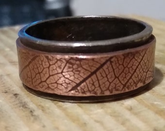Puede incluir: Un anillo de cobre con un diseño de hoja. El anillo está hecho de dos bandas, una de cobre y otra de plata.