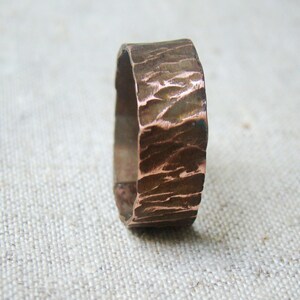 Puede incluir: Un anillo de cobre con un acabado martillado texturizado. El anillo es ancho y tiene una forma redondeada.