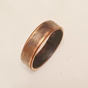 May include: A copper band ring with a hammered finish. The ring has a wide band and a smooth inner surface.