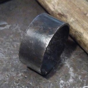 May include: A close-up of a silver metal ring on a gray textured surface. The ring is round and has a smooth, polished finish.