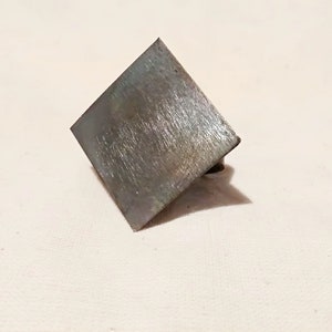 May include: A square metal plate with a brushed finish. The plate is slightly angled and has a small hole in the bottom right corner.