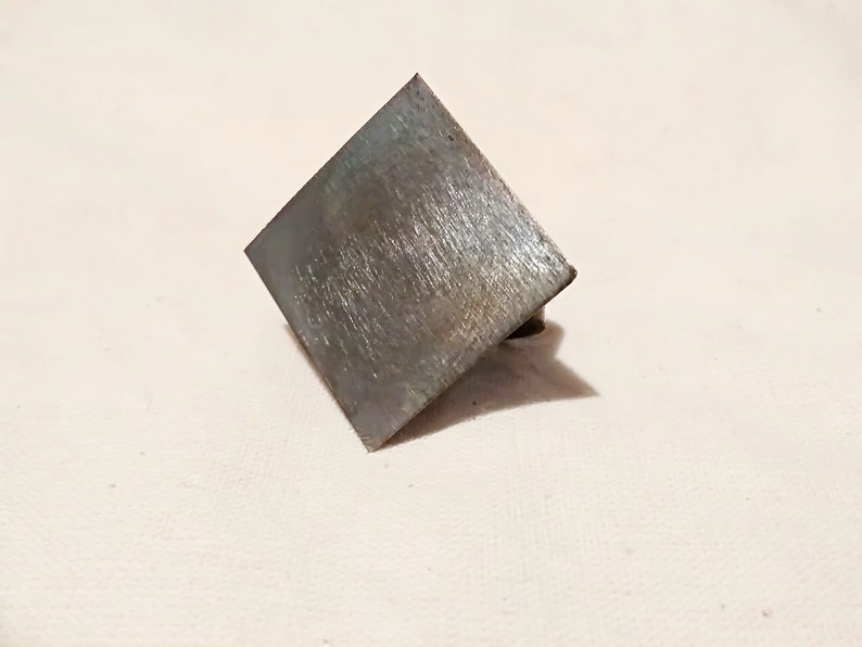 May include: A square metal plate with a brushed finish. The plate is slightly angled and has a small hole in the bottom right corner.