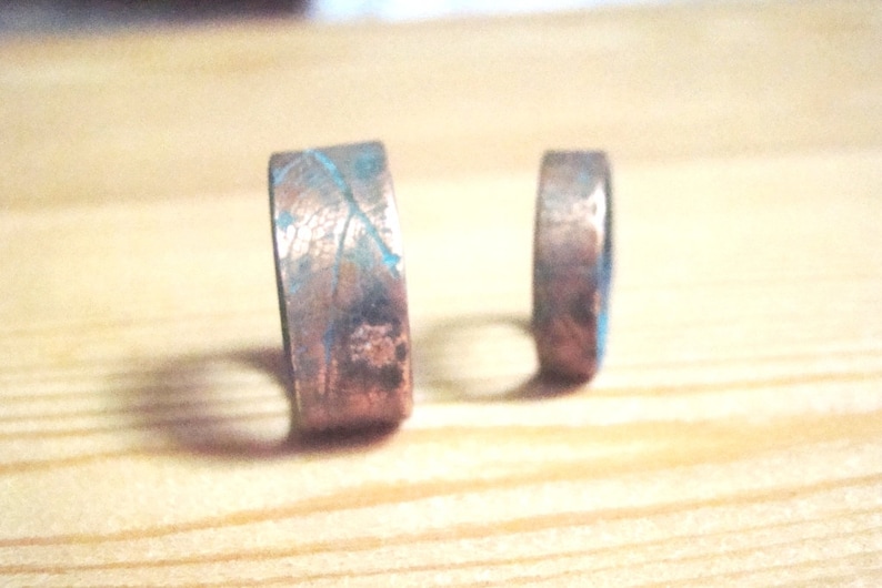 May include: Two copper rings with a textured surface and a blue patina. The rings are different sizes.