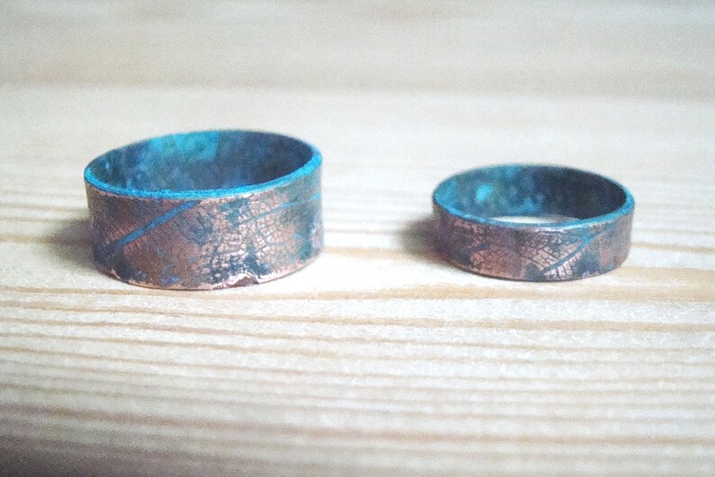 May include: Two copper rings with a blue patina finish. The rings have a textured surface that resembles a leaf pattern.
