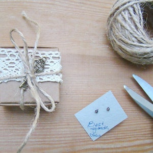 May include: A small brown box wrapped with twine and lace, tied with a key charm. The box is sitting on a wooden surface next to a card with the text "Best regards, Julia".