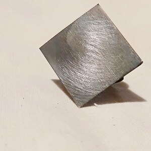 May include: A square-shaped metal object with a brushed silver finish. The object has a slightly textured surface and appears to be made of a durable material.