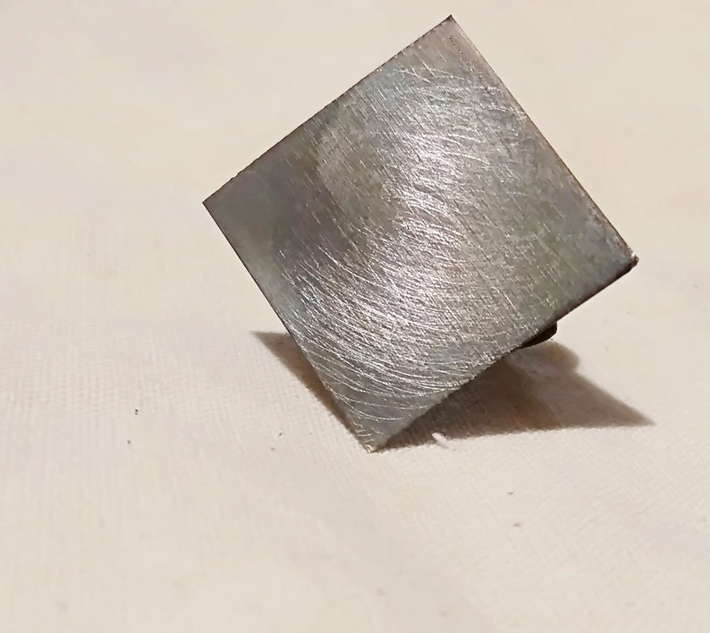 May include: A square-shaped metal object with a brushed silver finish. The object has a slightly textured surface and appears to be made of a durable material.