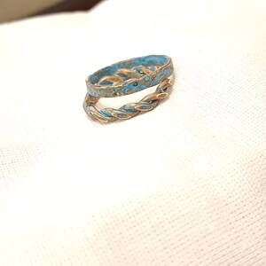 May include: A braided ring with a blue enamel finish. The ring is made of metal and has a twisted design.