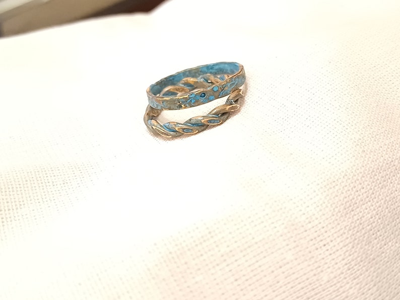 May include: A braided ring with a blue enamel finish. The ring is made of metal and has a twisted design.