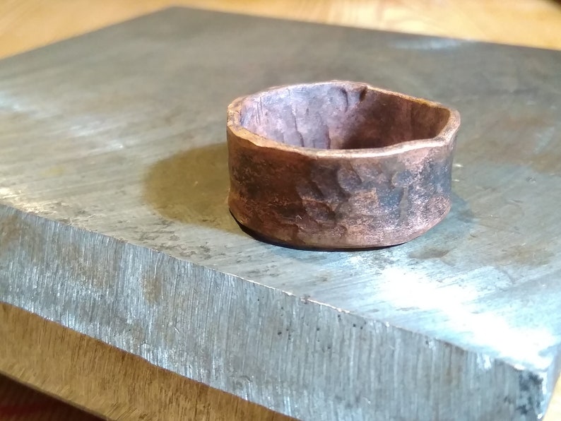 May include: A hammered copper ring with a rustic finish. The ring is thick and has a wide band.
