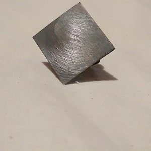 May include: A silver square-shaped metal object with a brushed finish.